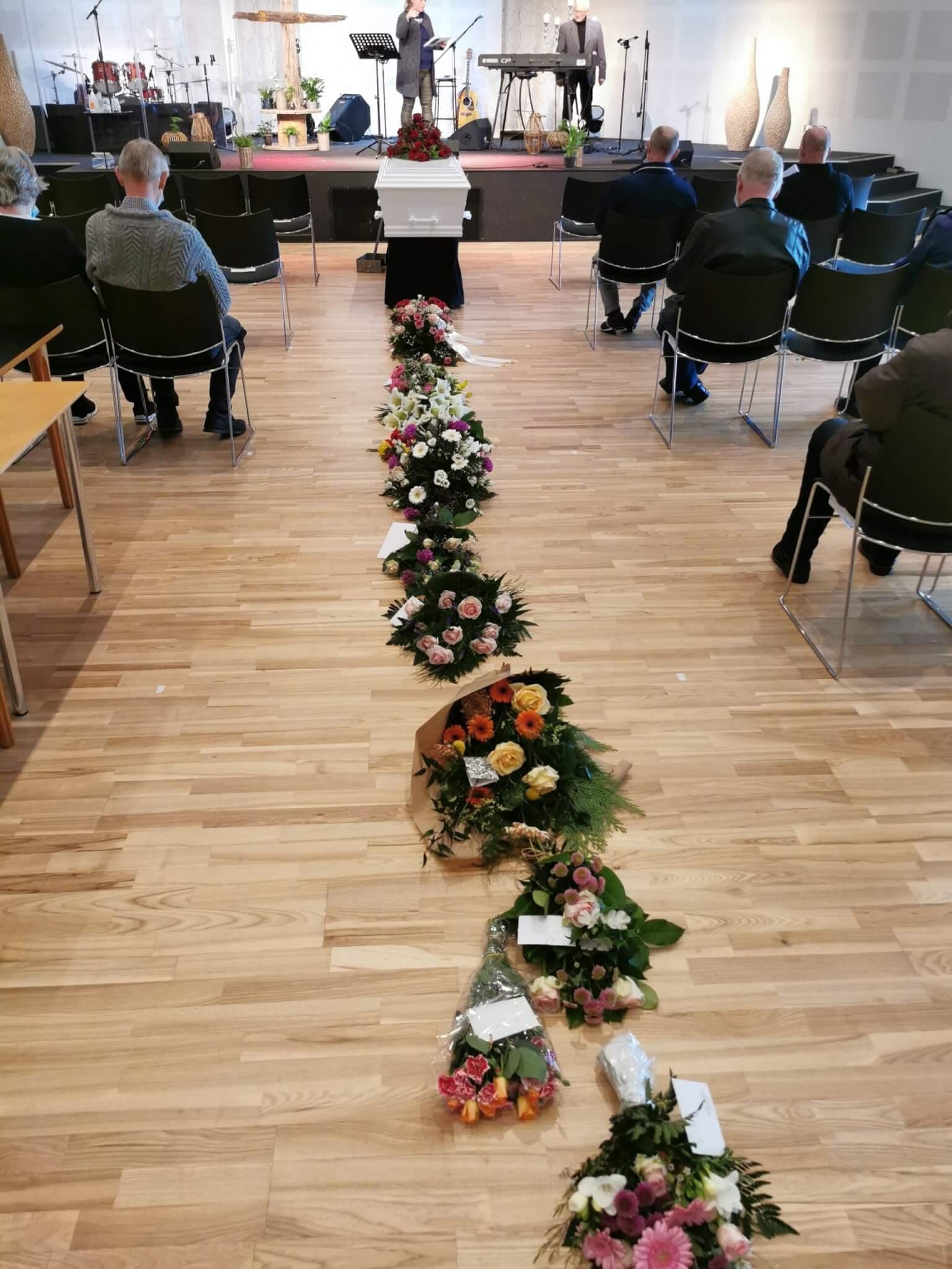 Un ataúd blanco con rosas rojas está delante del escenario en la sala de la iglesia