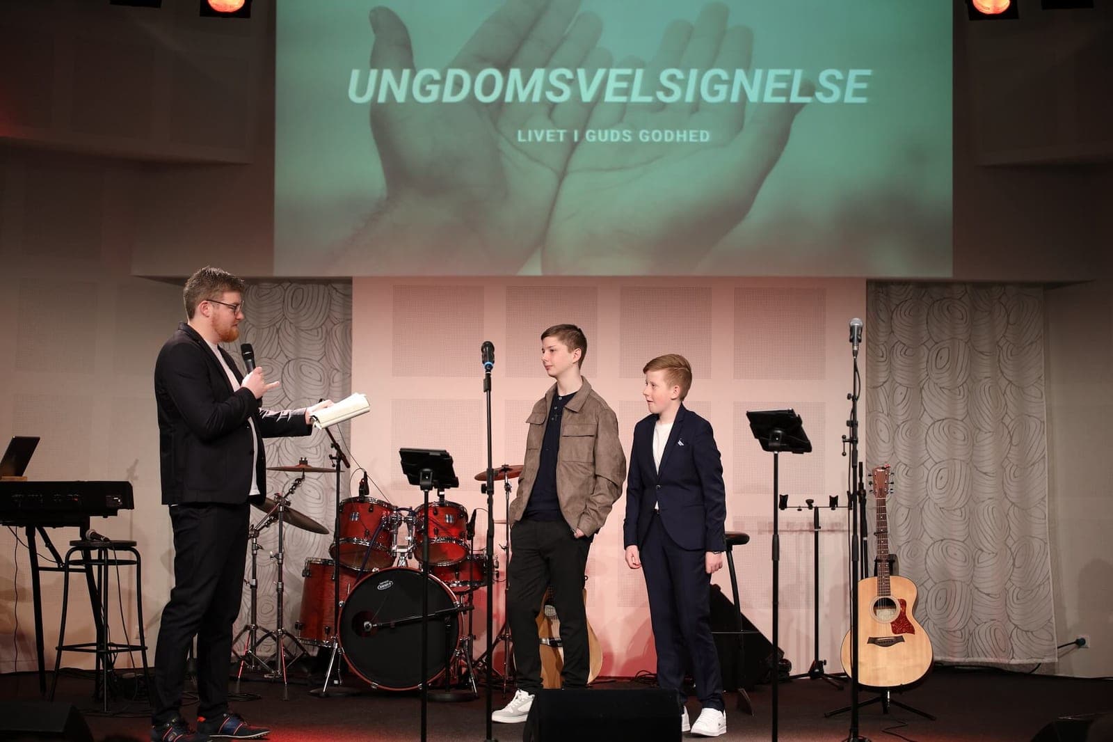 To unge står på scenen til ungdomsvelsignelse, mens præsten læser for dem